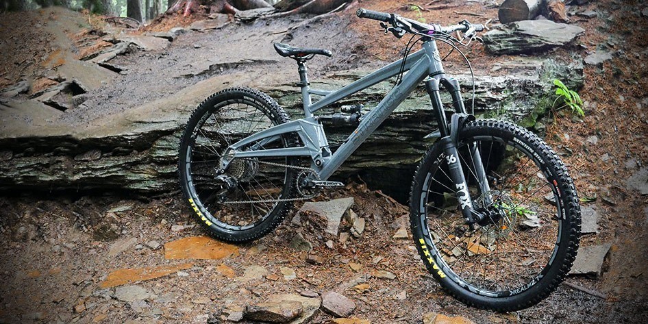 A Orange Alpine 6 MTB placed against a muddy slab of a rock in a woodland scene